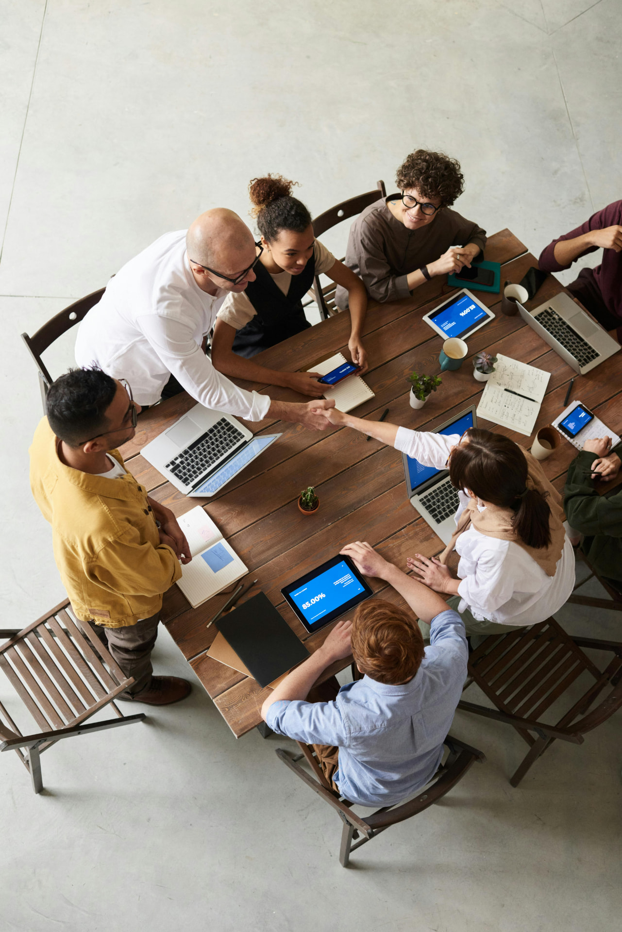 A team of five collaborating around a table, shaking hands over a shared plan